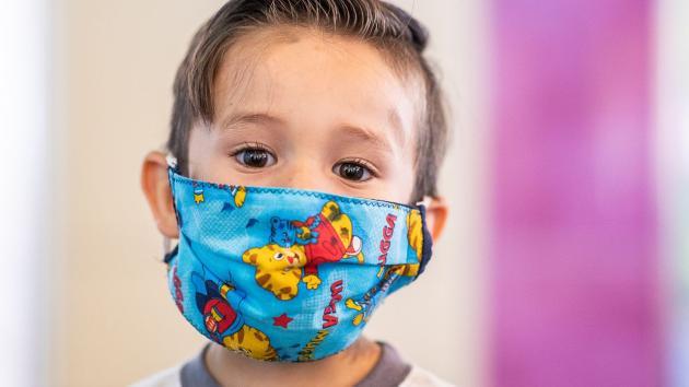 a Latino boy is wearing a teal colored facemask with cartoon characters in bright yellow and red